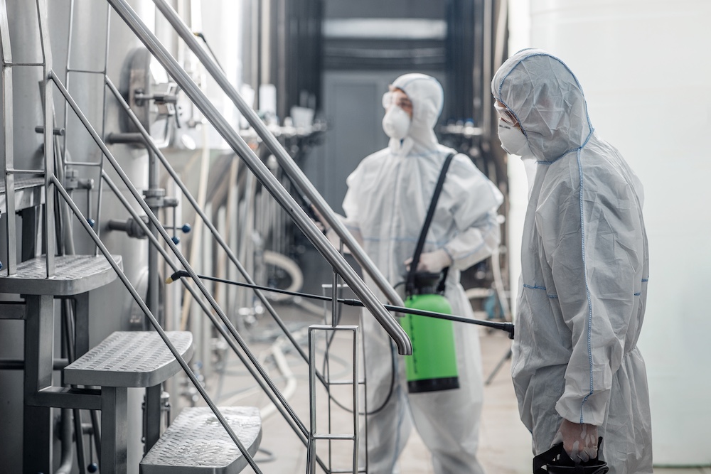 Cleaning and disinfection at work during quarantine. Guys in protective suits and glasses, work with spray bags in plant