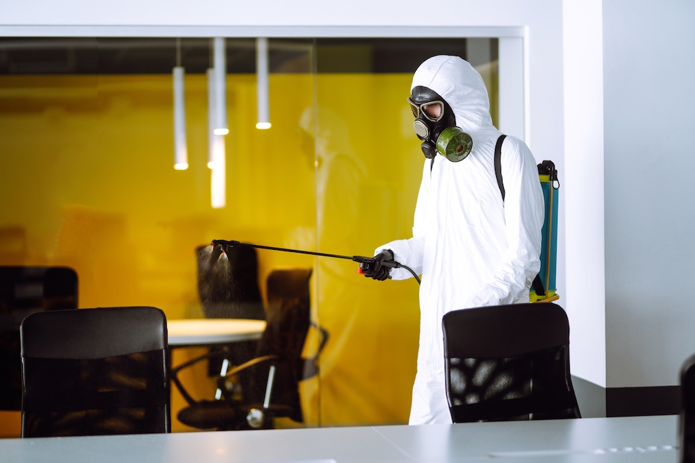 Disinfecting of office to prevent COVID-19, Man in protective hazmat suit with spray chemicals.